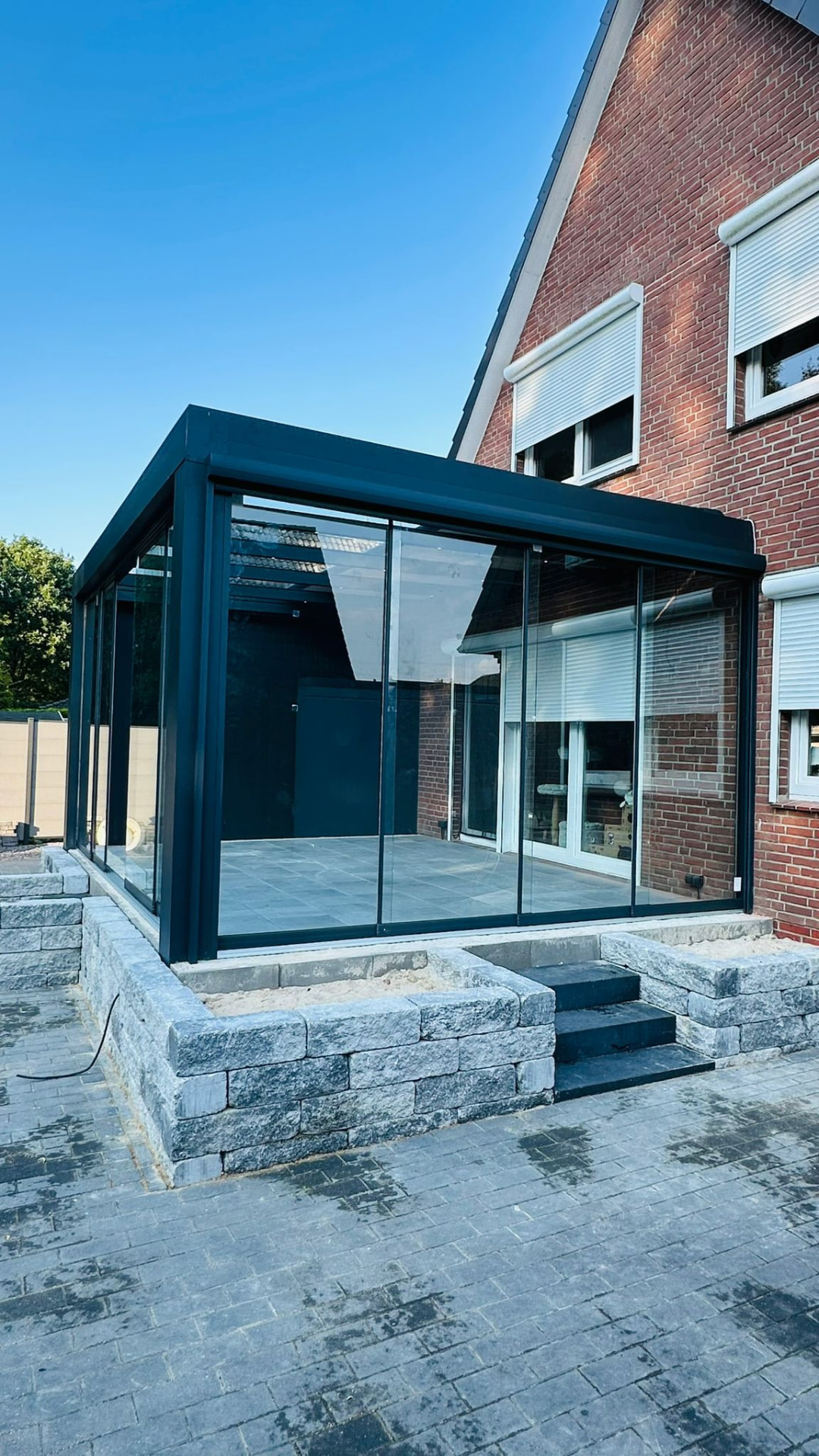 Cube Überdachung mit Glasschiebewänden auf einem Natursteinpodest