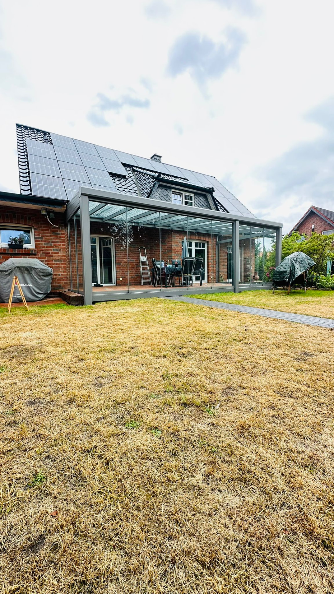 Terrassenüberdachung mit Glasdach und Glasschiebewänden vor einem Klinkerhaus