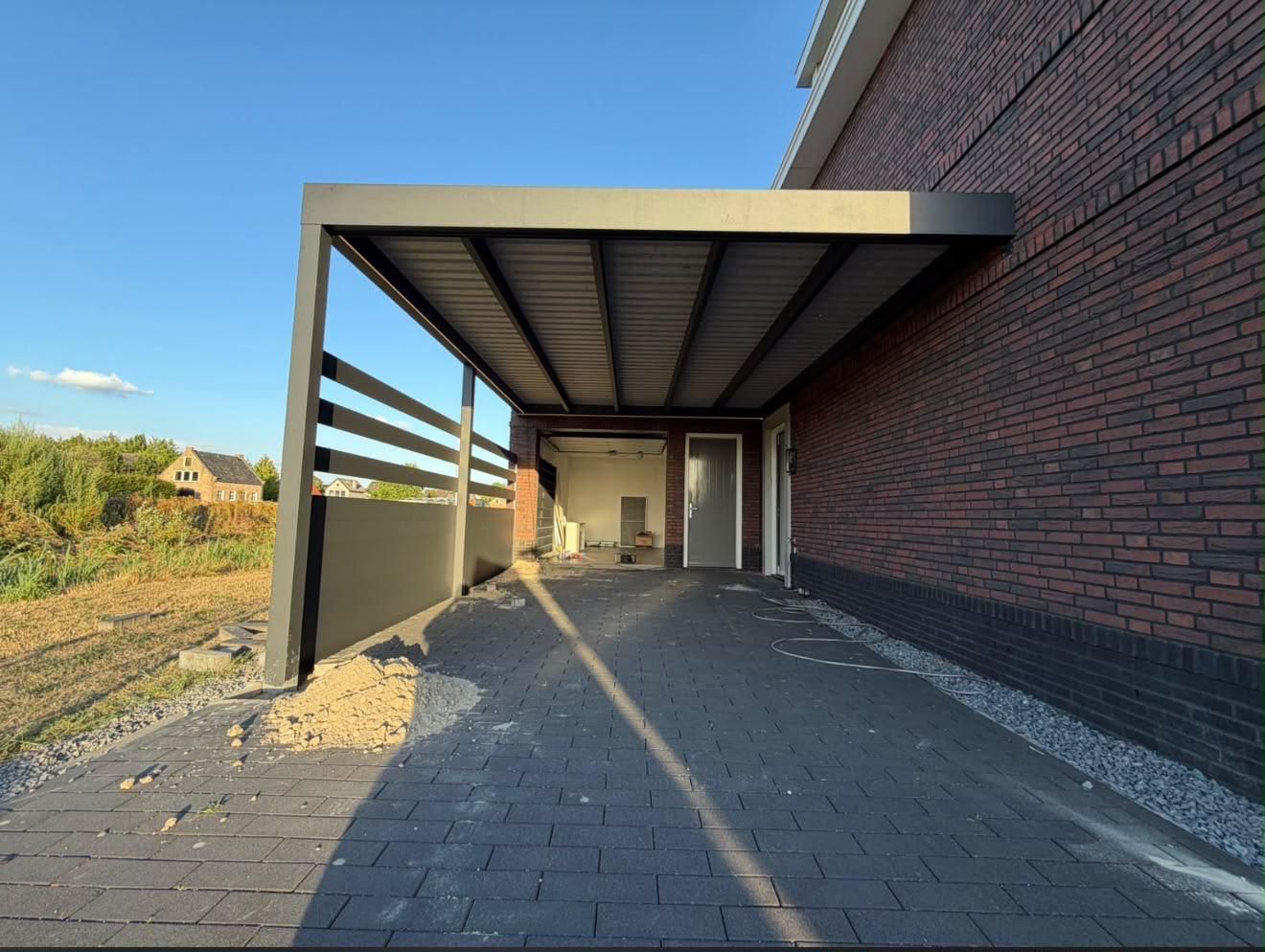 Carport mit Flachdach und Seitenwand neben einem Klinkerhaus