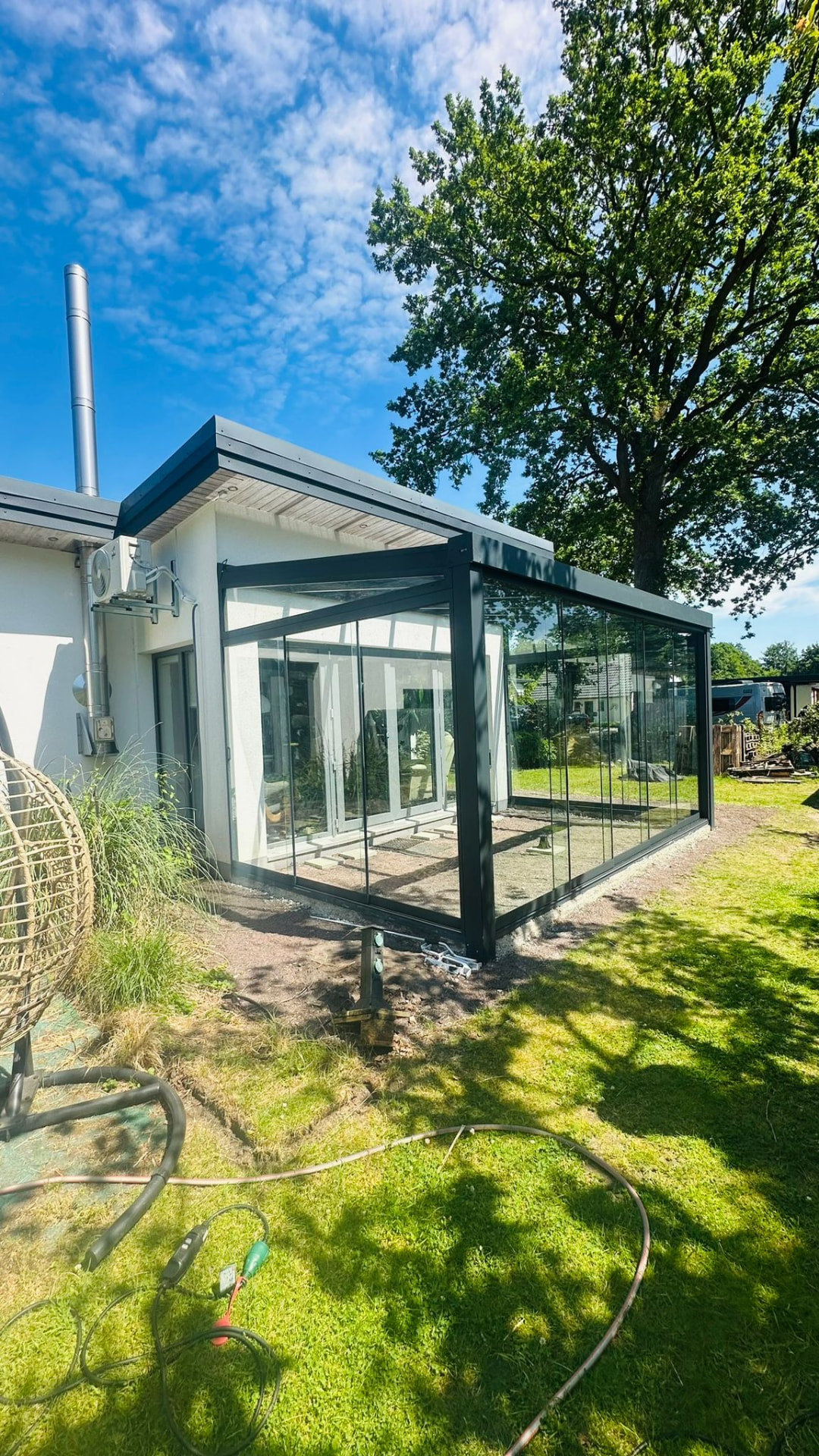 Terrassenüberdachung mit rahmenloser Verglasung an einem weißen Haus